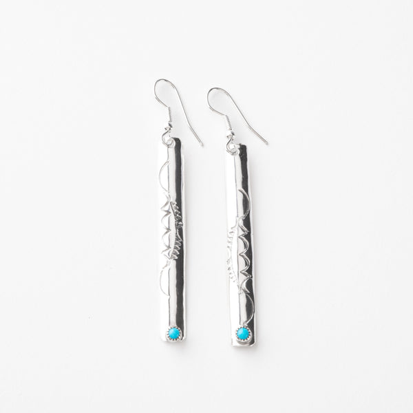 Pair of long silver earrings with turquoise stones on a white background