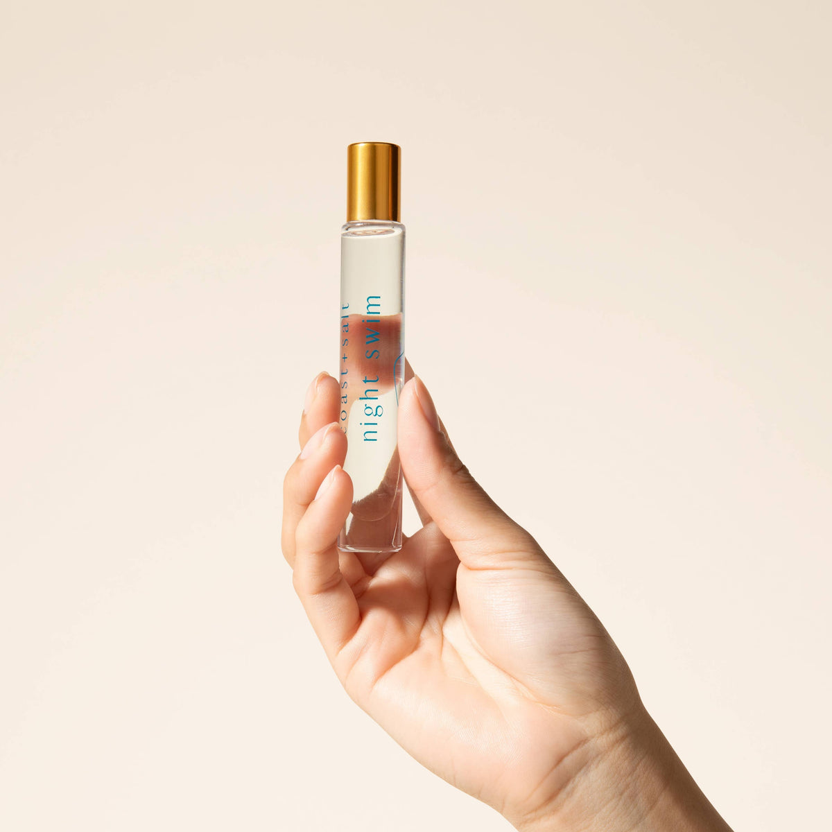 Hand holding a small perfume bottle labeled 'night swim' against a beige background