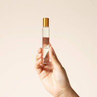 Hand holding a small perfume bottle with a gold cap against a beige background
