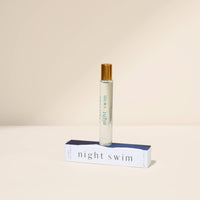 Roll-on bottle labeled 'night swim' with its box on a beige background