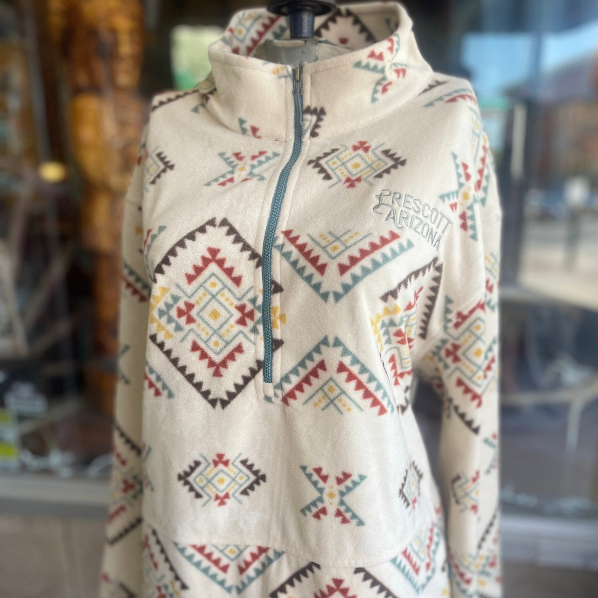 Beige fleece jacket with colorful geometric patterns on a mannequin against a blurred indoor background.