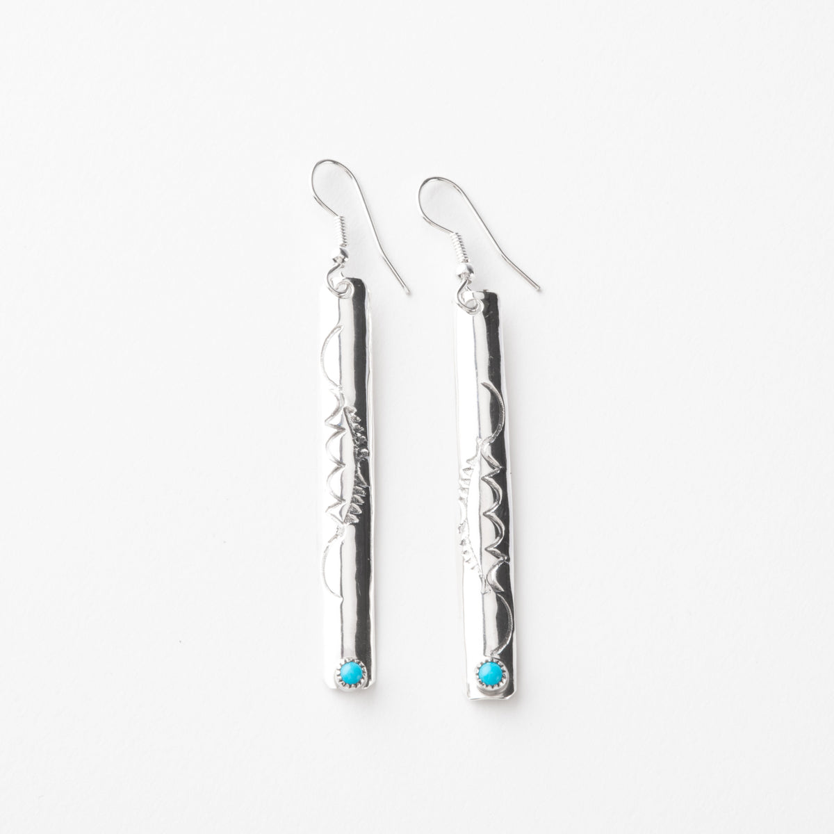 Pair of long silver earrings with turquoise stones on a white background