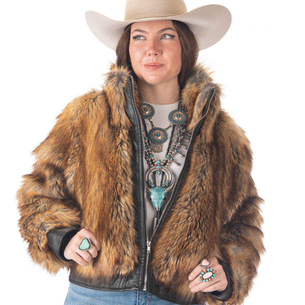 Woman wearing a fur jacket, cowboy hat, and turquoise jewelry on a white background