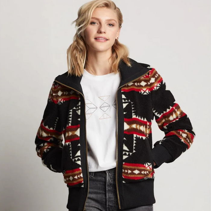 A woman wearing a black, red, and beige patterned bomber jacket with a stand collar, zip front closure, and two pockets.