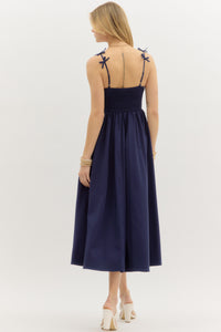 Navy: Solid twist front top pullover midi dress featuring bow accented adjustable shoulder strap. Smocked back closure. Lined. Woven. Non-sheer. Lightweight.