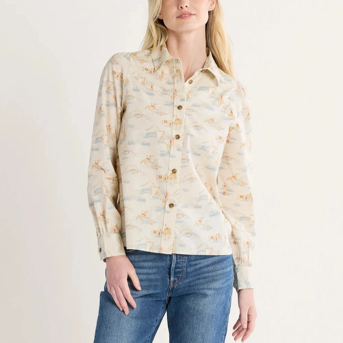 A woman wearing a long-sleeved blouse with a vintage-inspired cowboy print, buttoned front, and puff-sleeves. She is also wearing blue jeans.