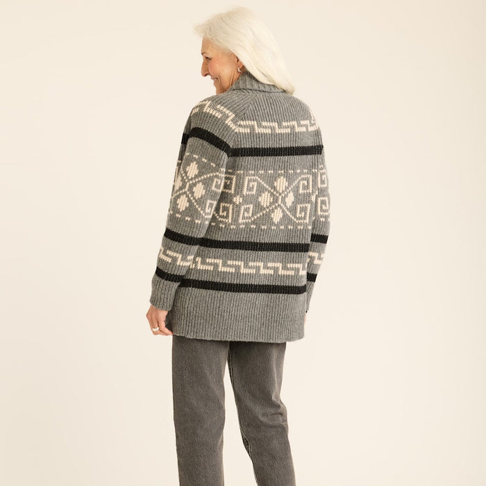 A woman facing away from the camera wears a long, geometric-patterned Pendleton cardigan in gray, black, and white, paired with gray trousers and black shoes.