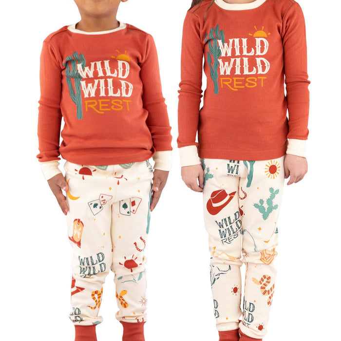 Two children, a boy and a girl, wearing matching long sleeve orange pajama sets with a western theme, including cowboy hats and campfire graphics.