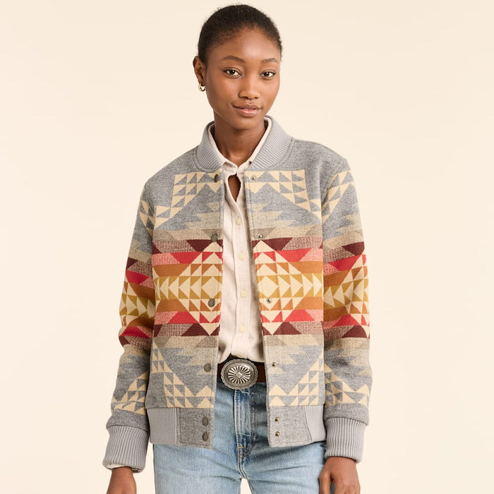 A woman wearing a multicolored geometric patterned Pendleton wool bomber jacket with snap closures and collar, paired with a white shirt and blue jeans.