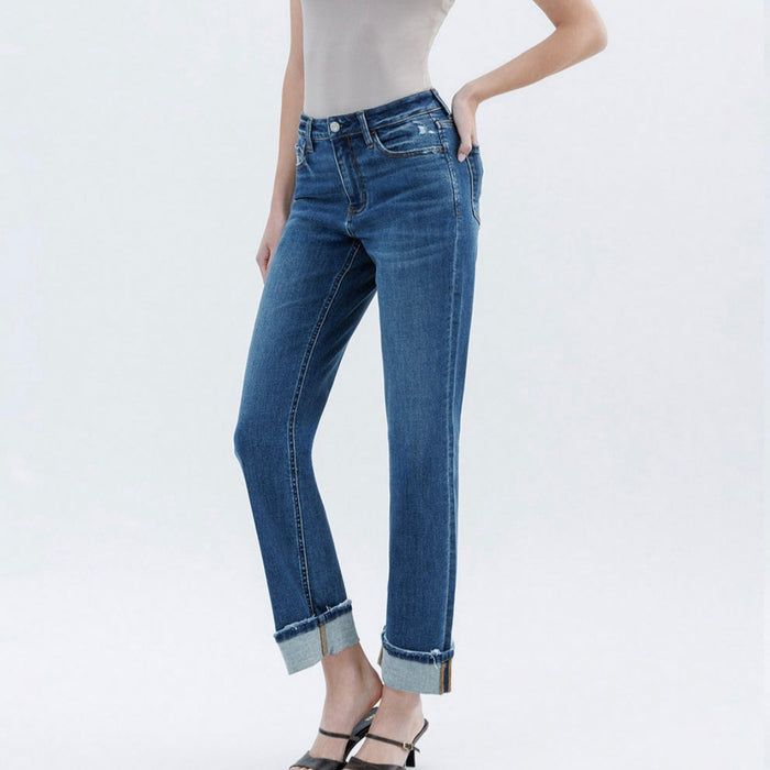 A female model wearing high-rise straight-leg blue jeans with a single cuff and a white tank top.