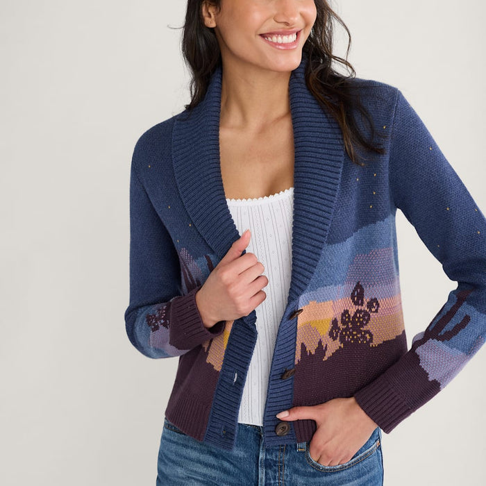 A woman smiling and wearing a multicolored western scenic cotton cardigan with a desert scene at night, featuring cacti silhouetted against a dark starry sky.