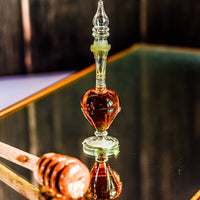 Glass honey dipper with honey on a reflective surface