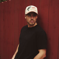 Man wearing a cap and black t-shirt against a red wooden fence