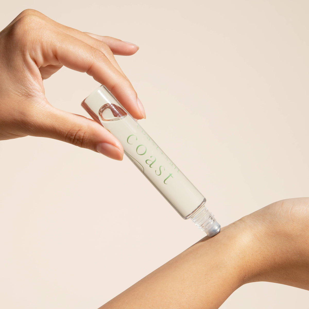 Hand holding a white cosmetic tube labeled 'Coast' against a beige background