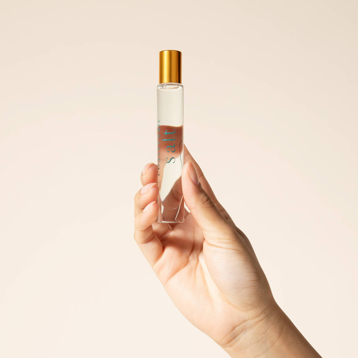 Hand holding a perfume bottle with a gold cap against a beige background