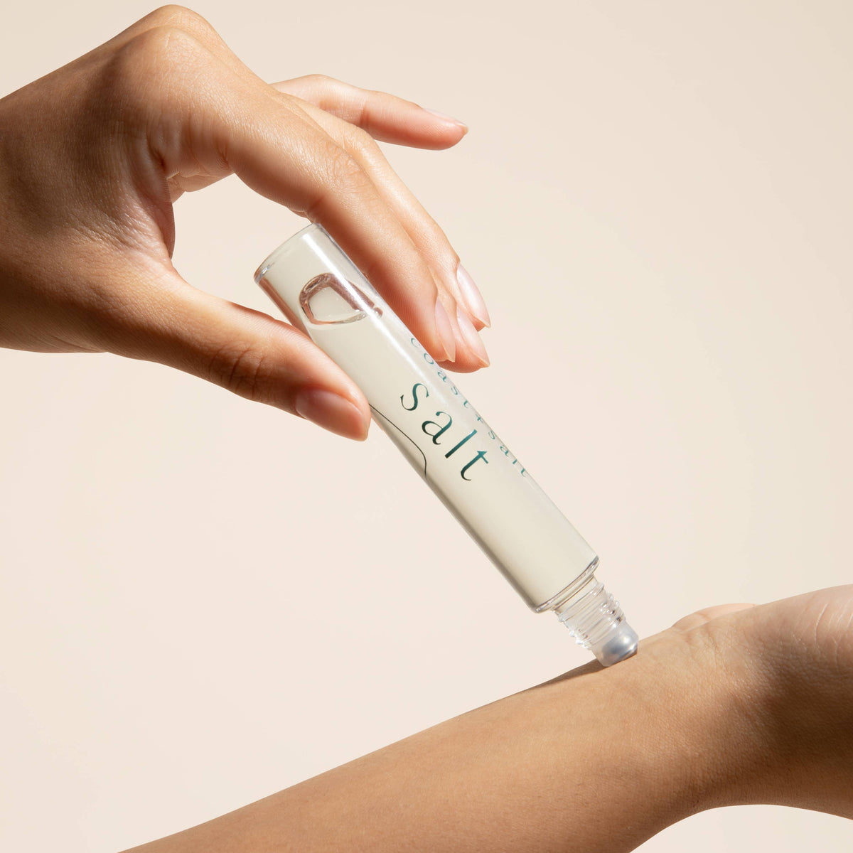 Hand applying a skincare product labeled 'salt' to a person's arm on a beige background